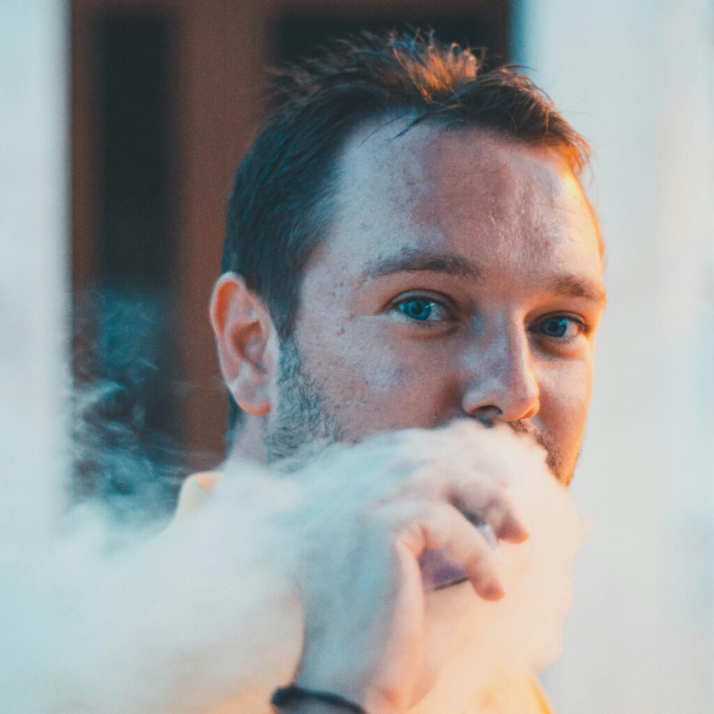 Close-up portrait of a man vaping with a dramatic smoke effect and selective focus.